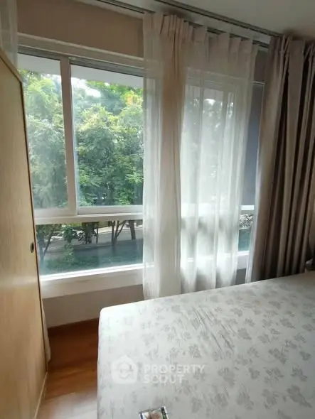 Cozy bedroom with large window offering lush green view