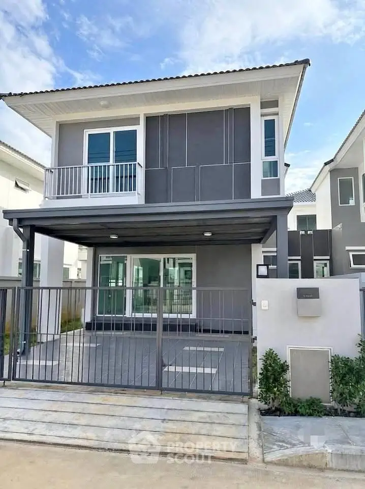 Modern two-story house with balcony and gated driveway in a suburban neighborhood.