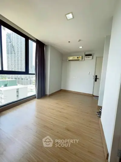 Spacious modern room with large window and city view, featuring sleek wooden flooring and air conditioning.