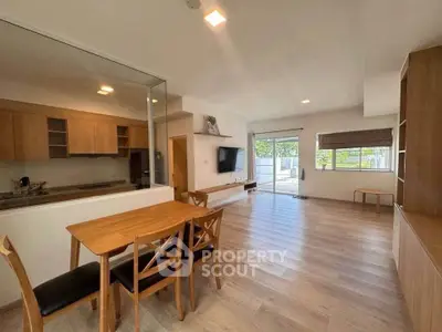 Spacious open-plan living room with modern kitchen and dining area, featuring large windows and wooden flooring.