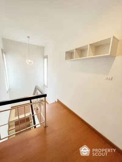 Bright and airy upper-level space with elegant chandelier, wooden flooring, and a unique wall-mounted shelving unit, perfect for modern living.