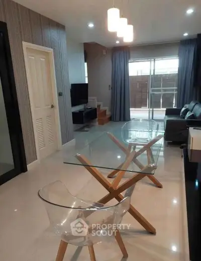 Modern living room with glass table and transparent chairs, featuring stylish decor and natural light.