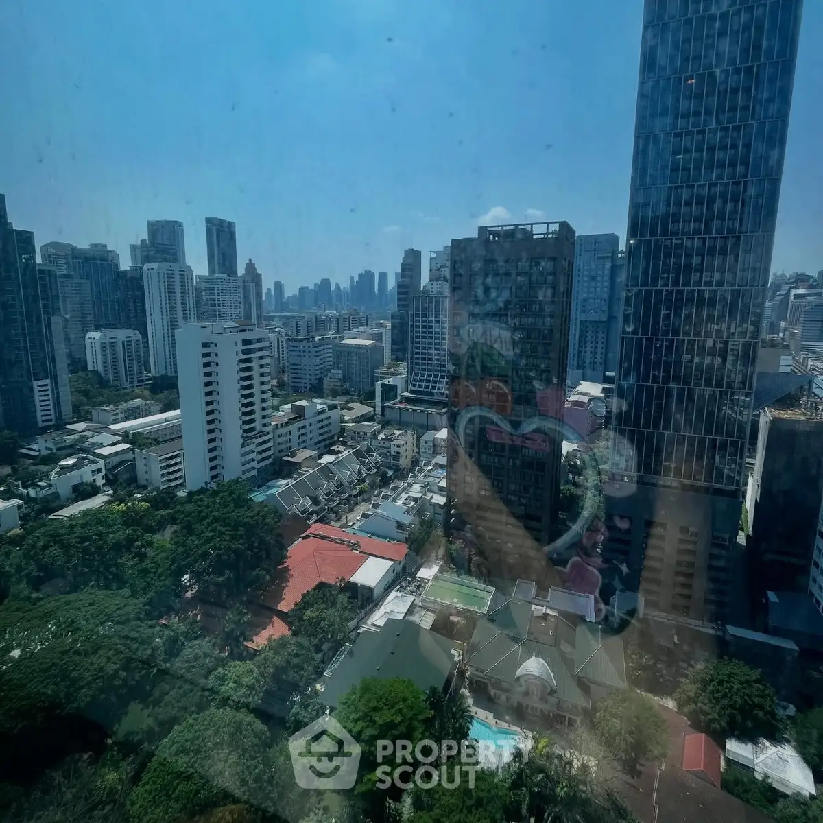 Stunning cityscape view from a high-rise building showcasing urban skyline and lush greenery.