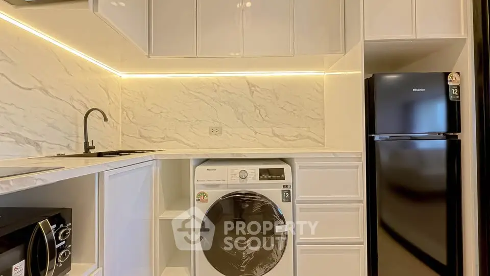 Modern kitchen with sleek appliances and marble backsplash, featuring a washing machine and fridge.