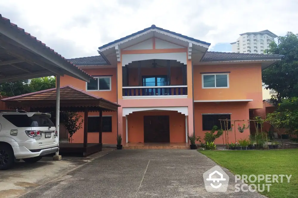 Charming two-story peach house with carport and lush garden in suburban setting.