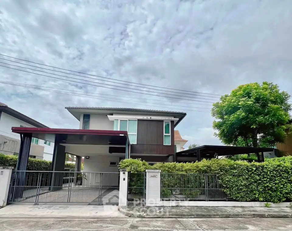 Modern two-story house with gated driveway and lush greenery in a serene neighborhood.