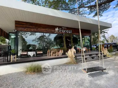 Charming modern cafe with glass facade and outdoor swing in lush forest setting.