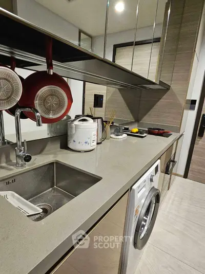 Modern kitchen with sleek countertops, built-in washing machine, and stylish hanging pans.