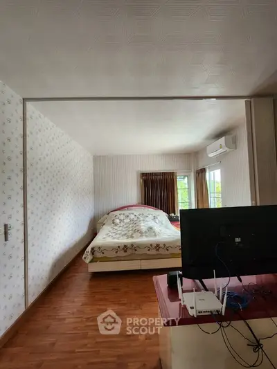 Cozy bedroom with floral wallpaper and wooden flooring, featuring a bed and a TV setup.