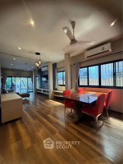 Spacious living room with wooden flooring, modern ceiling fan, and red dining chairs in a well-lit interior.