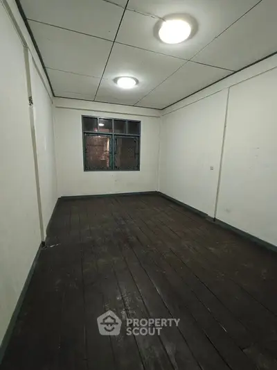 Spacious empty room with wooden flooring and window, ideal for customization.