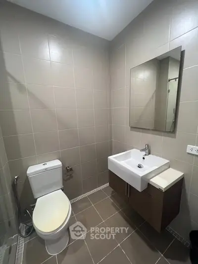 Modern bathroom with sleek fixtures and neutral tiles, featuring a wall-mounted sink and toilet.