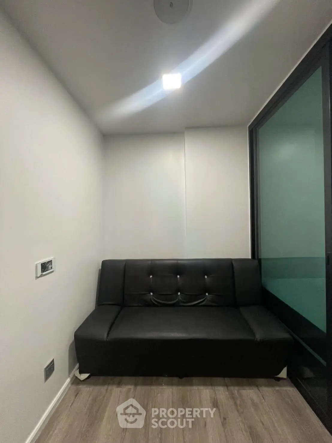 Cozy small living room with modern black sofa and sleek wooden flooring.