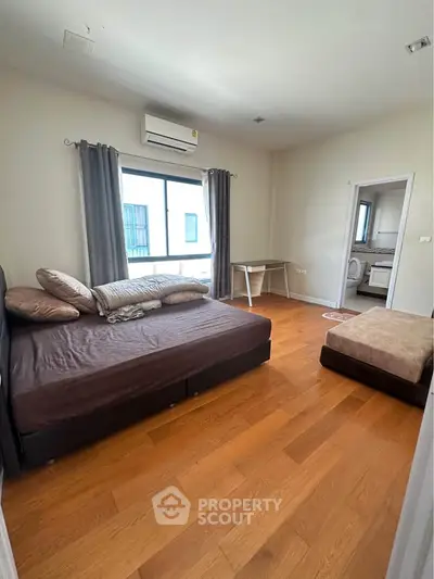 Spacious bedroom with wooden flooring, large window, and modern furnishings in a stylish apartment.