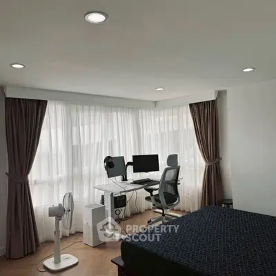 Modern bedroom with study area featuring a sleek desk, ergonomic chair, and large windows with curtains.