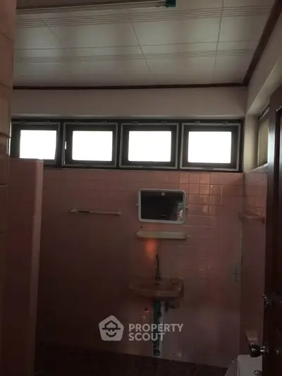Cozy bathroom with pink tiles and natural light from high windows.