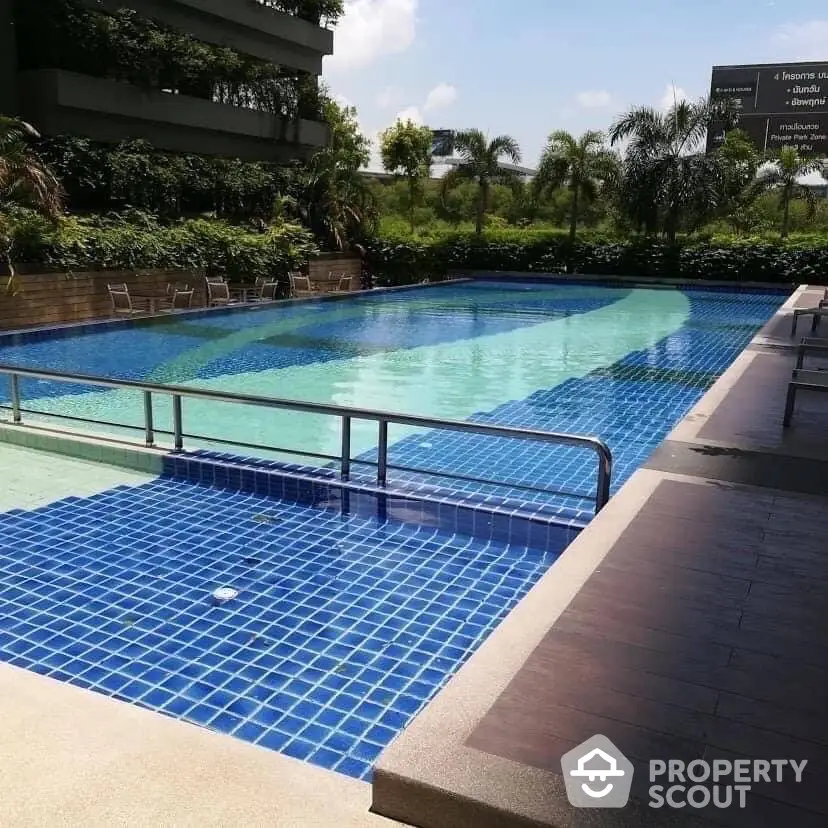 Luxurious outdoor swimming pool with lush greenery and clear blue sky, perfect for relaxation and leisure.