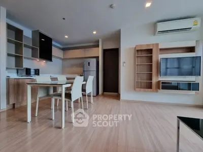 Modern open-layout living room with sleek kitchen and dining area, featuring contemporary furniture and appliances.