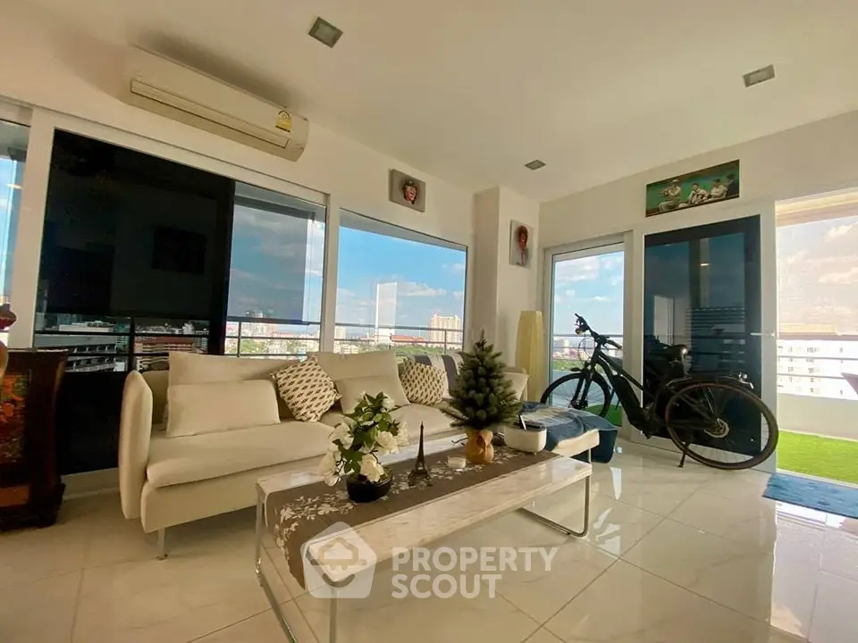 Modern living room with large windows and city view, featuring a white sofa and decorative plants.
