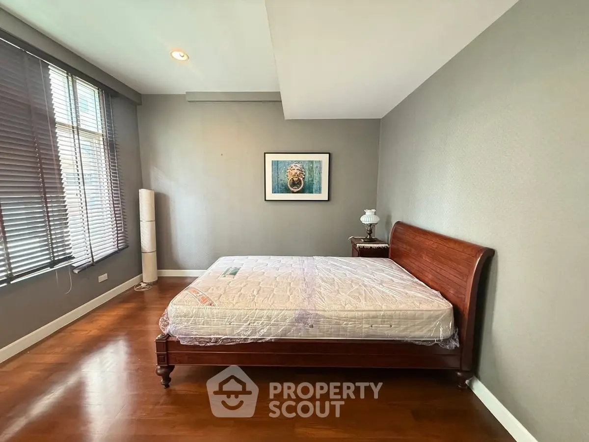 Spacious bedroom with wooden flooring and elegant bed frame, featuring large windows for natural light.