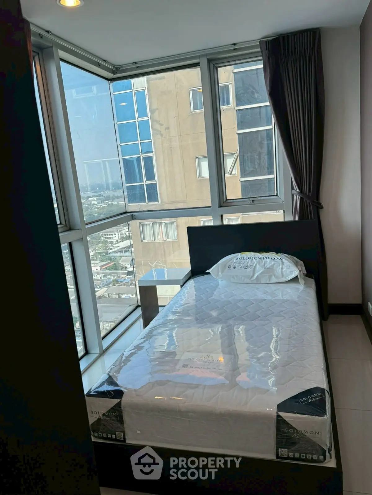 Modern bedroom with large windows offering city views in a high-rise apartment.