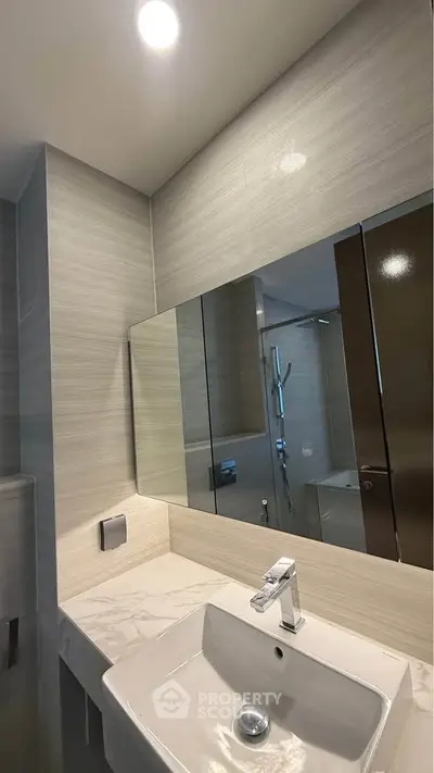 Modern bathroom with sleek sink and large mirror, featuring elegant tile design.