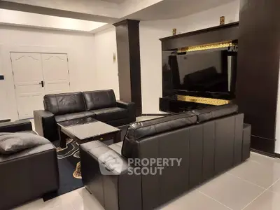 Luxurious modern living room with sleek black leather sofas and large flat-screen TV.