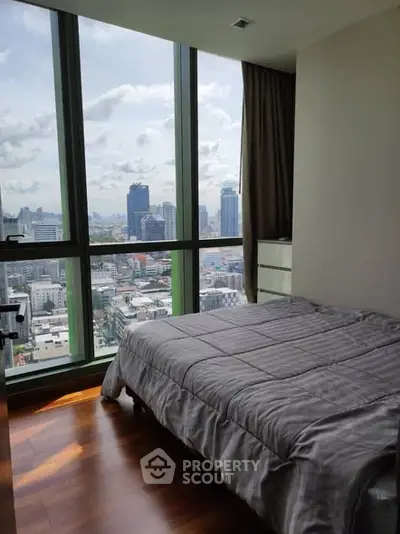 Modern bedroom with stunning city view through floor-to-ceiling windows, featuring cozy bed and wooden flooring.
