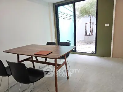 Modern dining area with wooden table and chairs, large glass door opens to a small patio garden.