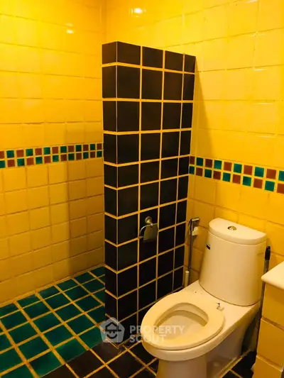 Vibrant yellow tiled bathroom with modern toilet and unique design.