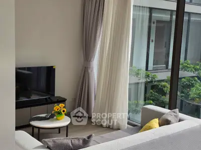 Bright living room with large windows and modern decor, offering a serene view of greenery.