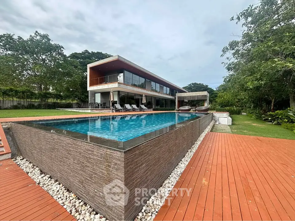 Luxurious modern home with stunning pool and expansive deck surrounded by lush greenery.