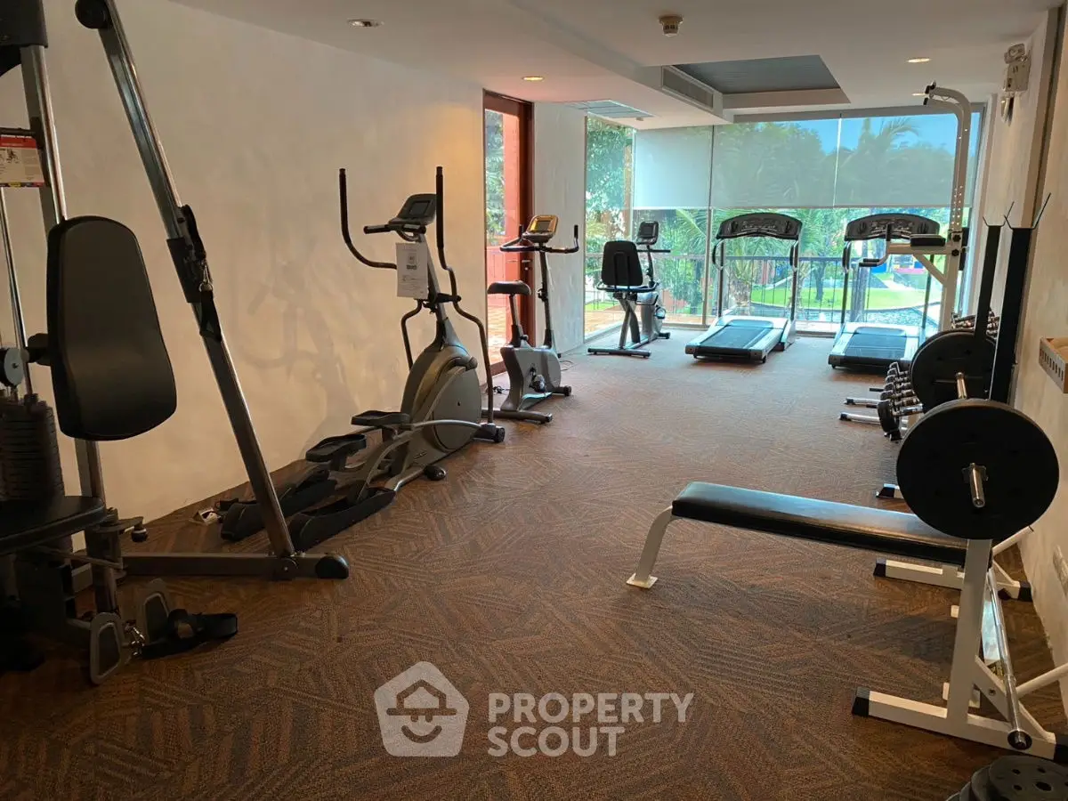 Spacious gym with modern equipment and pool view in luxury residential complex.