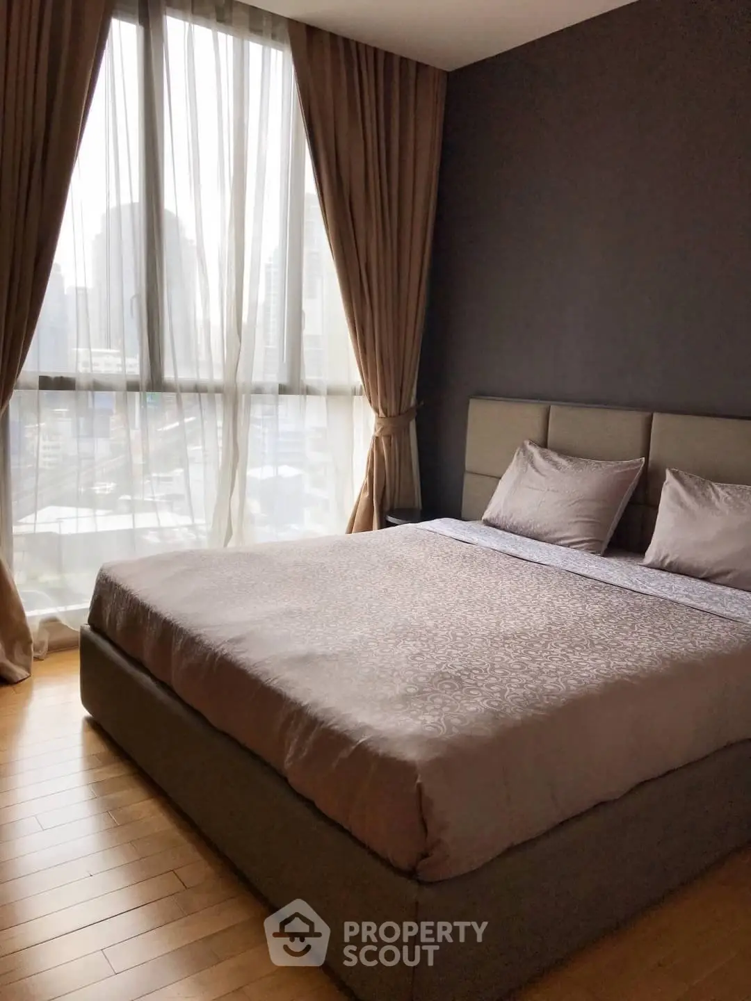 Spacious bedroom with large window offering city views, featuring a cozy bed and elegant curtains.