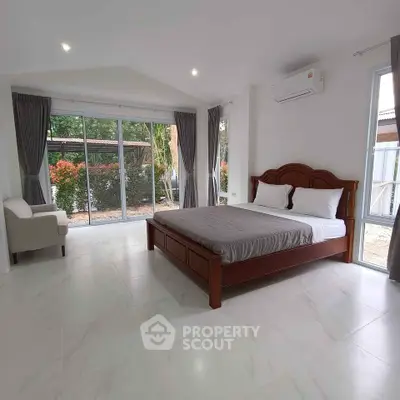 Spacious bedroom with large windows and garden view, featuring modern decor and ample natural light.