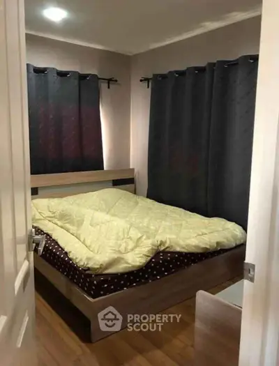Cozy bedroom with wooden flooring and dark curtains, featuring a comfortable bed.