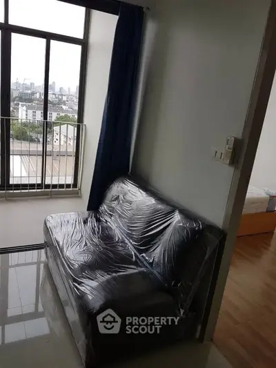 Cozy apartment with city view and compact living area, featuring a plastic-covered sofa and adjacent bedroom.