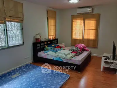 Cozy bedroom with wooden flooring and ample natural light, featuring a comfortable bed and air conditioning.