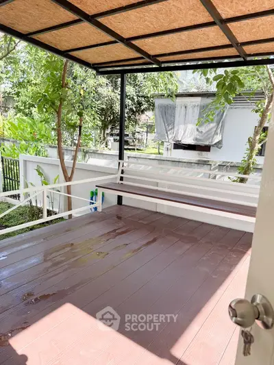 Charming garden view from a cozy balcony with wooden flooring and lush greenery.