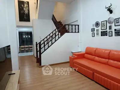 Spacious living room with modern decor and vibrant orange sofa, featuring elegant staircase and stylish wall art.
