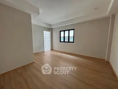 Spacious empty room with wooden flooring and large window, perfect for customization.