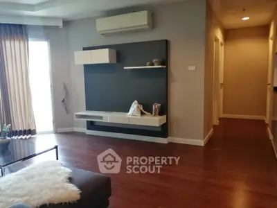 Spacious living room with polished hardwood floors, modern wall-mounted entertainment unit, and ample natural light filtering through sheer curtains.