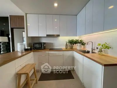 Modern kitchen with sleek white cabinets and wooden countertops, featuring a cozy open layout.
