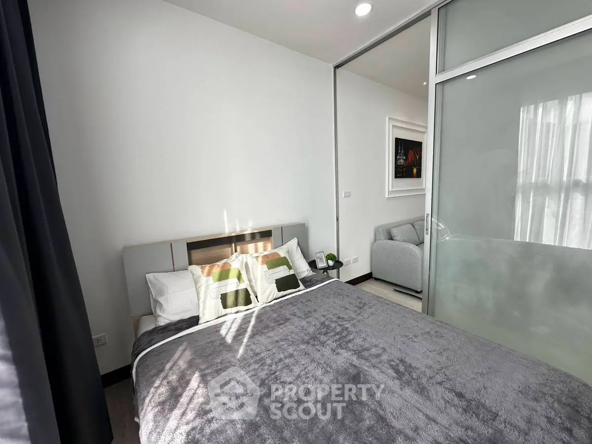 Modern bedroom with cozy bed and sliding glass door leading to a stylish living area.