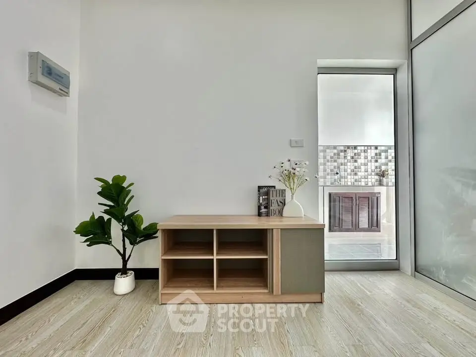 Modern minimalist interior with wooden cabinet and potted plant, featuring sleek glass door and stylish decor.