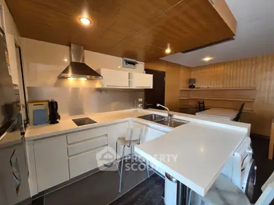 Modern kitchen with sleek white cabinets and open layout, featuring a breakfast bar and integrated appliances.
