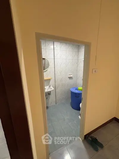 Compact bathroom with tiled walls and floor, featuring a small sink and a blue storage bin.