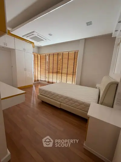 Spacious bedroom with modern design, wooden flooring, and ample natural light from large windows.