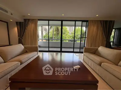 Spacious living room with large windows and garden view, featuring elegant sofas and a wooden coffee table.