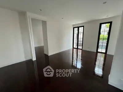 Spacious empty living room with dark hardwood floors and large windows.